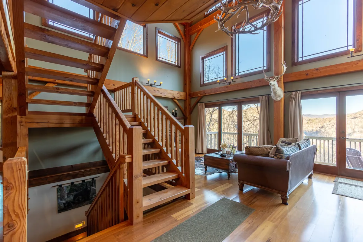 A comfortable seating area with plush chairs, a view of the staircase, and large windows that frame the scenic outdoors. The antler chandelier and fireplace add mountain lodge character, while the arrangement is perfect for group relaxation or lively conversation after a day exploring Banner Elk.