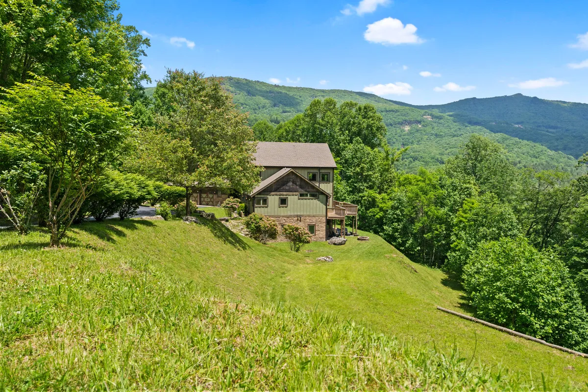 A welcoming home nestled amid tall trees with a stunning mountain backdrop. The house is surrounded by ample green space, making it an inviting environment for outdoor games, family gatherings, and exploration.