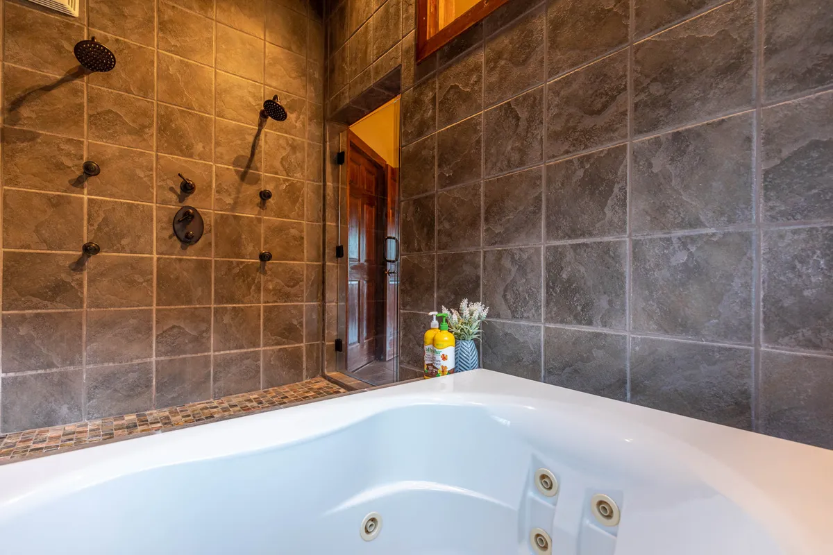 A luxurious bathroom showcasing a jacuzzi tub and modern shower fixtures set against textured wall tiles. The space evokes a spa-like experience, perfect for unwinding after a busy day of adventure.