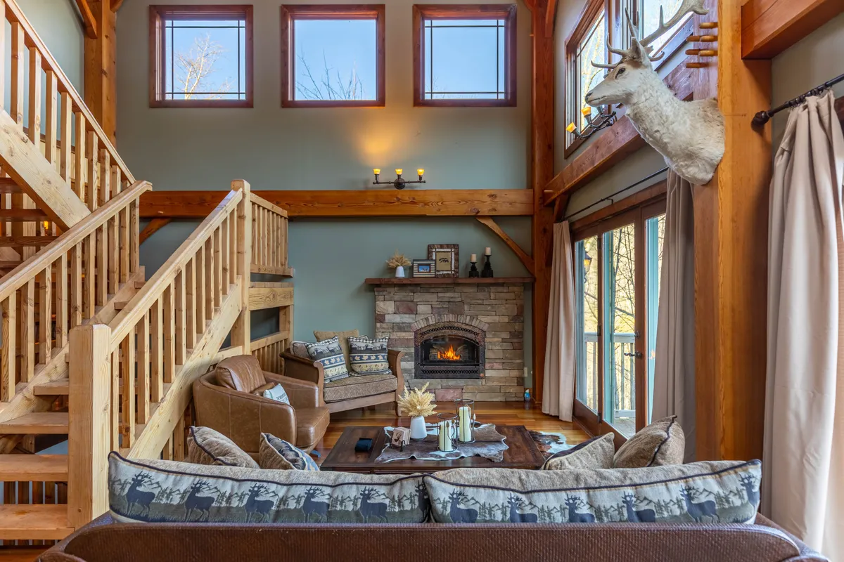 A living area with a commanding stone fireplace, cozy seating arranged for conversation, a staircase, and large windows framing mountain views. The setting is perfect for relaxing by the fire or enjoying the scenery after a day outdoors.