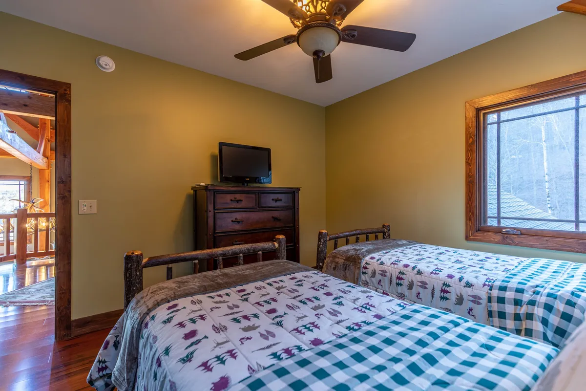 A family-friendly bedroom with twin beds, a wooden ceiling fan, and a window that offers a glimpse of the outdoors. The space is bright and relaxed, ideal for kids or friends to share restful nights and morning light.