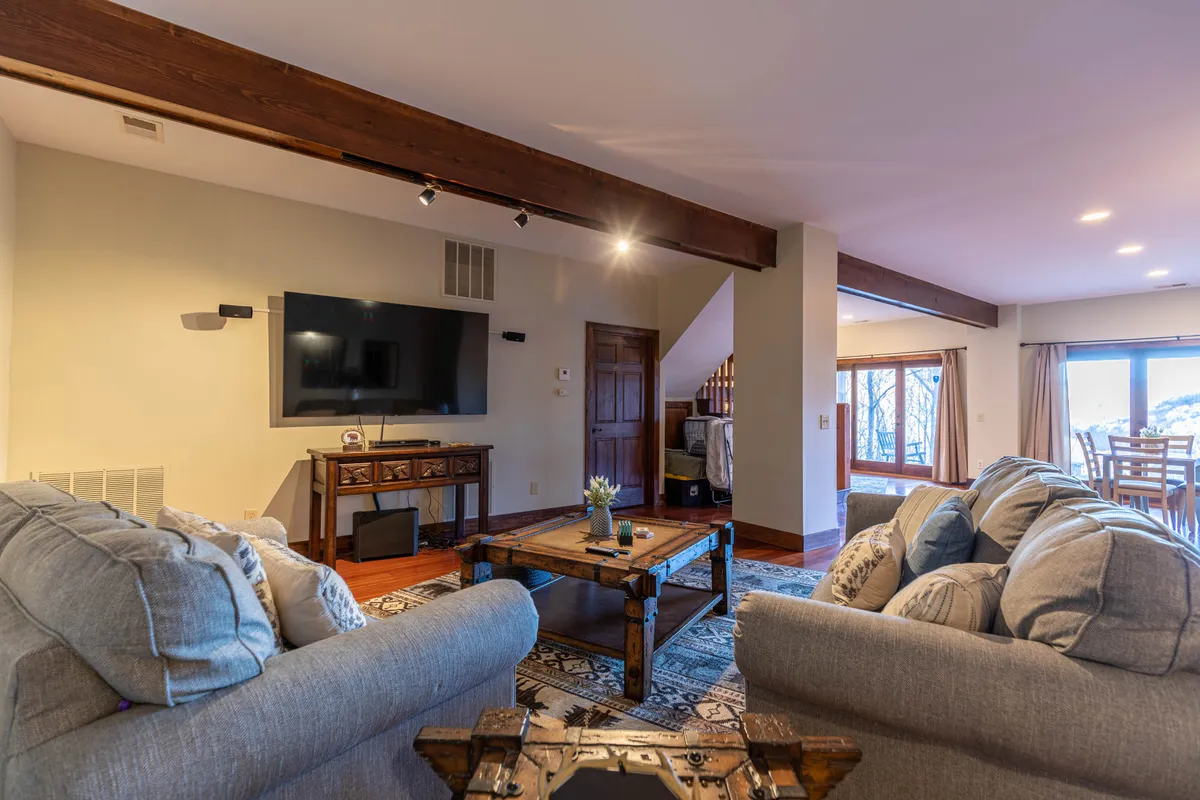 An open-concept lounge featuring comfortable sofas, a wooden coffee table ideal for group games, and a large TV positioned for optimal viewing. Large windows fill the room with natural light, highlighting both the leisure and entertainment aspects of the space.