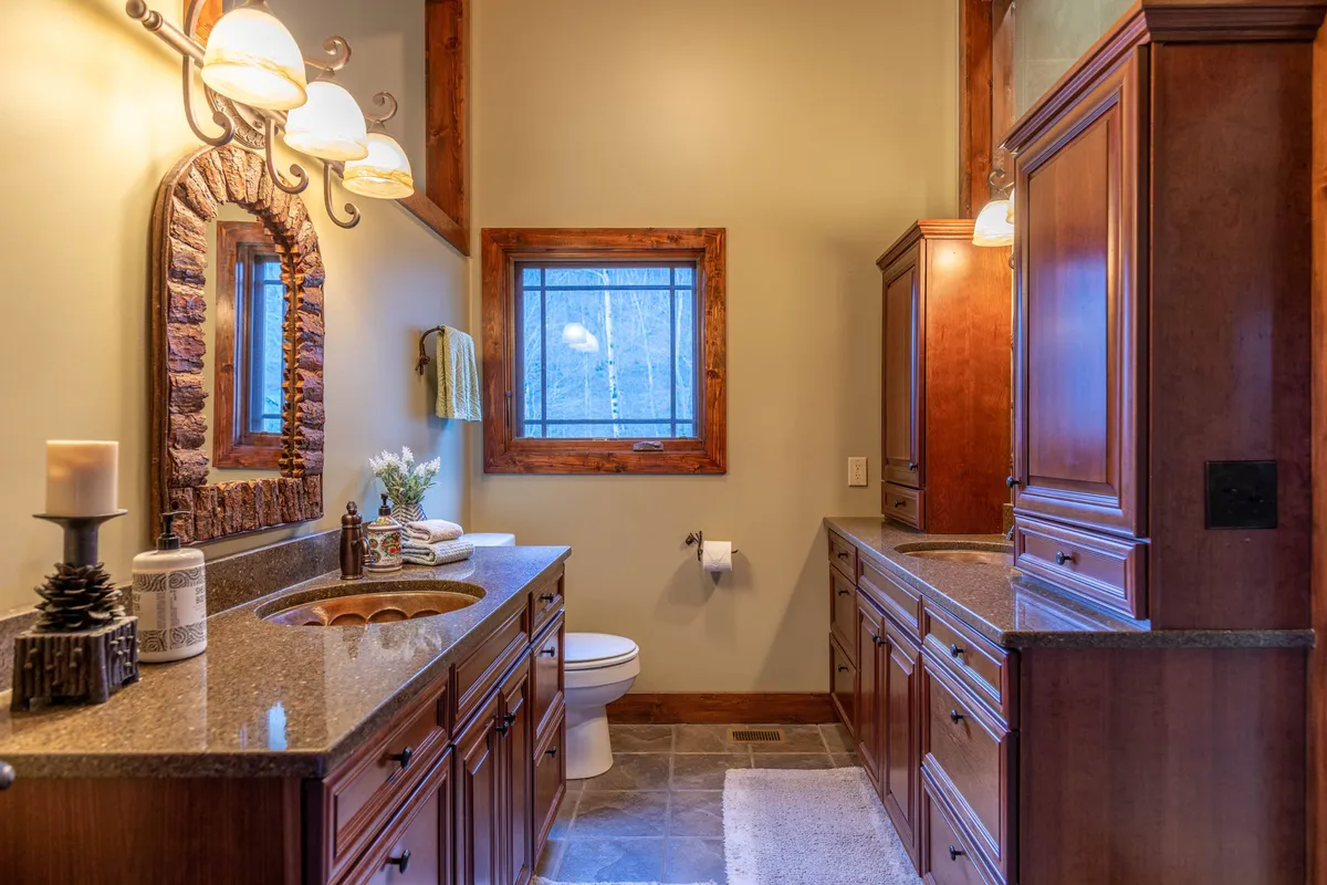 A serene bathroom space featuring a double sink vanity with a framed mirror and a window view. The area is designed for morning routines and self-care, emphasizing comfort and convenience for guests.