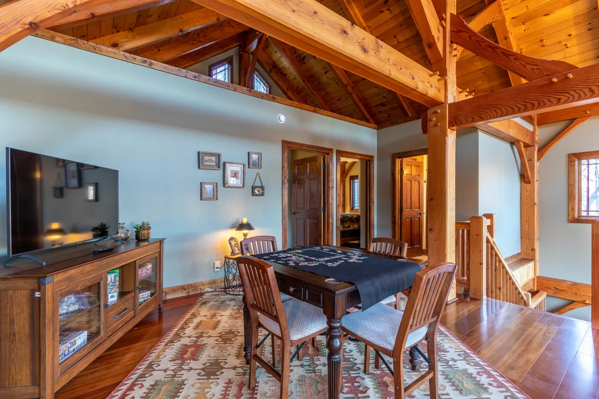 An inviting interior with a dining table set for games, a wall-mounted television, exposed wooden beams, and decorative touches that add warmth to the space. The combination of TV and open tabletop hints at versatile uses for both eating and entertainment.
