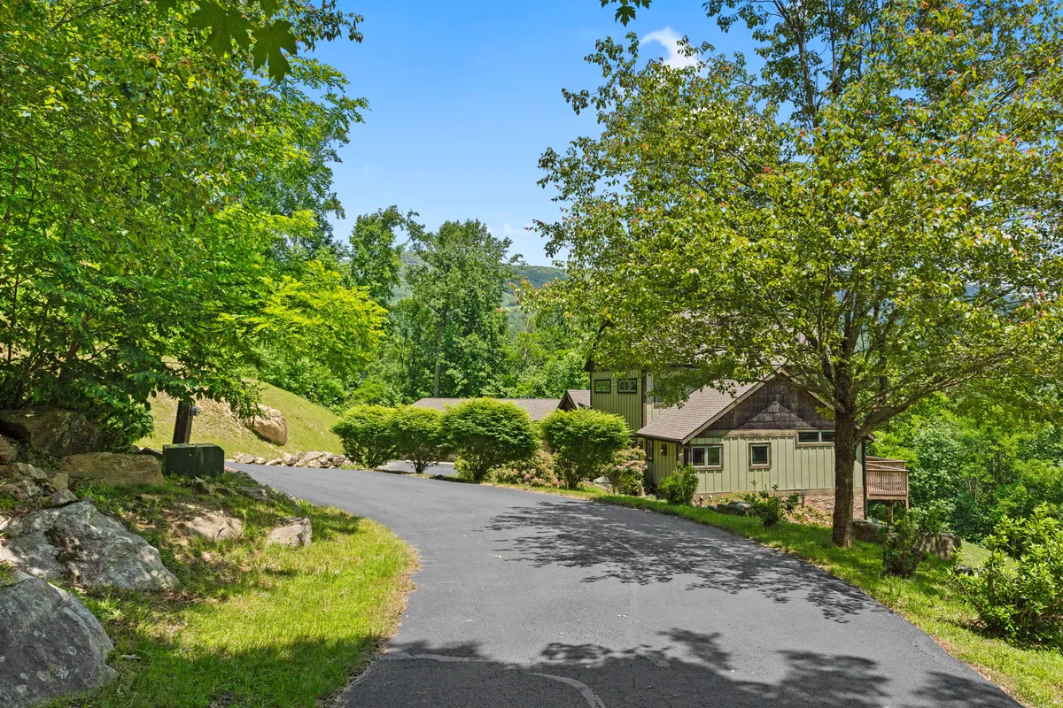 This exterior image features a tranquil scene with a house partially visible through a lush canopy of trees, a winding driveway, and a welcoming porch. The environment feels peaceful, natural, and perfectly integrated with the surrounding landscape, hinting at the proximity to outdoor adventure.