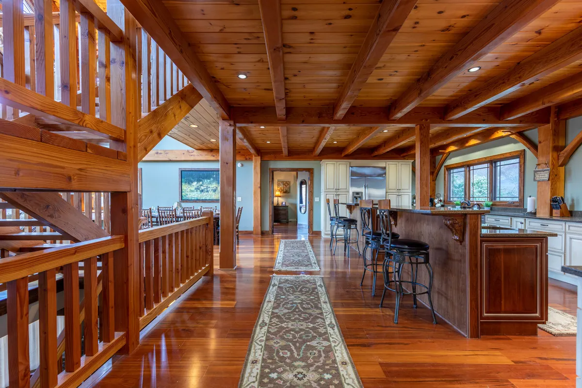 A warm, inviting interior scene showcasing the kitchen with wooden beams, a spacious island, and large windows. The layout suggests space for gatherings, meal preparation, and entertaining. Natural light pours in, creating a cozy yet refined atmosphere.