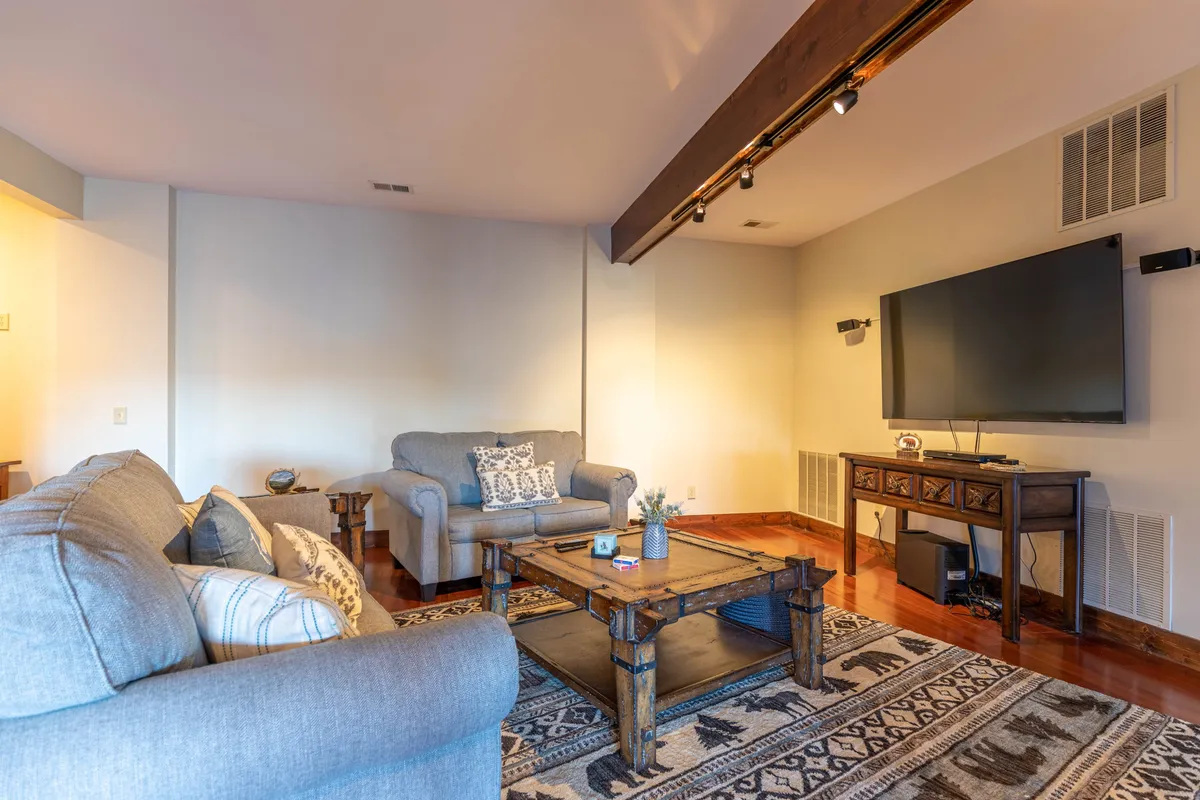 A cozy living area featuring a plush sofa, a coffee table set up for games, and a large television on the wall. The room is tastefully decorated, with natural light streaming in from side windows, creating an inviting space perfect for family activities and relaxation.