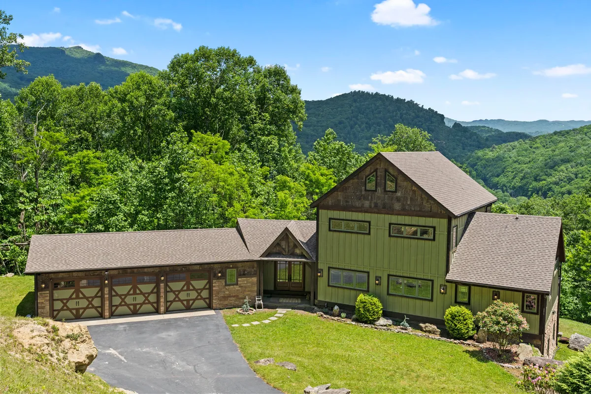 This image captures the exterior of the home framed by surrounding trees and set against a striking mountain backdrop. The house appears welcoming and spacious, with natural landscaping that hints at tranquility and privacy. The setting sun bathes the scene in a warm glow, enhancing the sense of peaceful escape.
